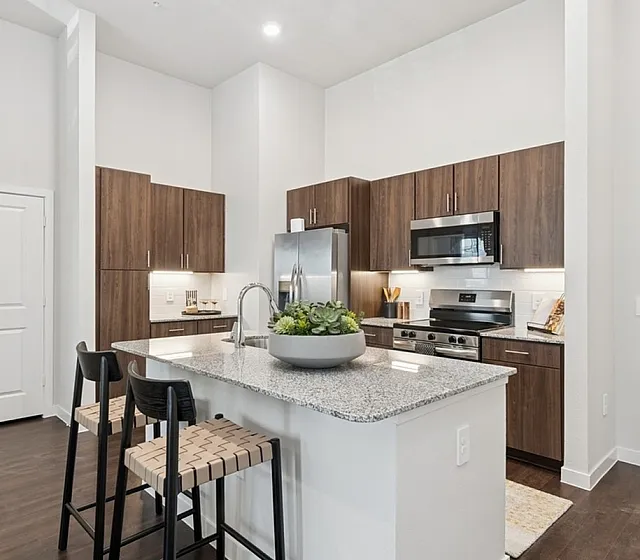 Modern kitchen with elegant dark wood cabinets, a sleek island with granite countertop, and contemporary bar stools in a bright open space.