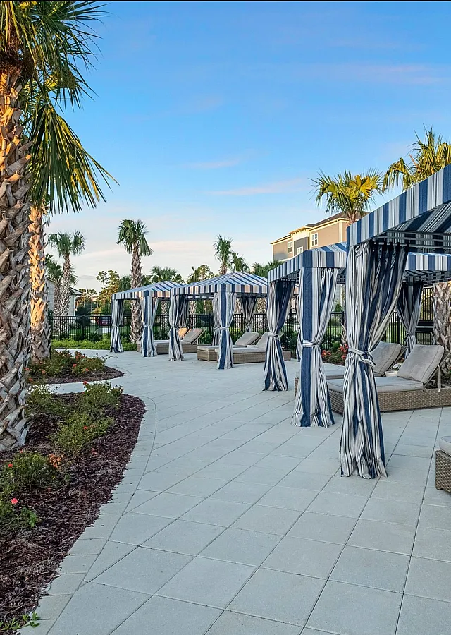 Luxurious outdoor poolside area with elegant striped cabanas, surrounded by lush palm trees and vibrant landscaping.