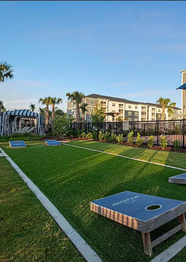 Inviting apartment community exterior with lush landscaping, palm trees, and a playful outdoor area featuring a bocce ball court.
