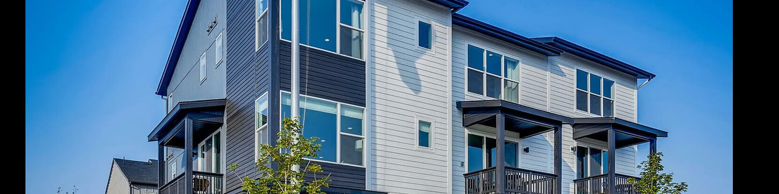 Modern three-story townhouse with large windows and balconies, featuring sleek dark and light gray siding.