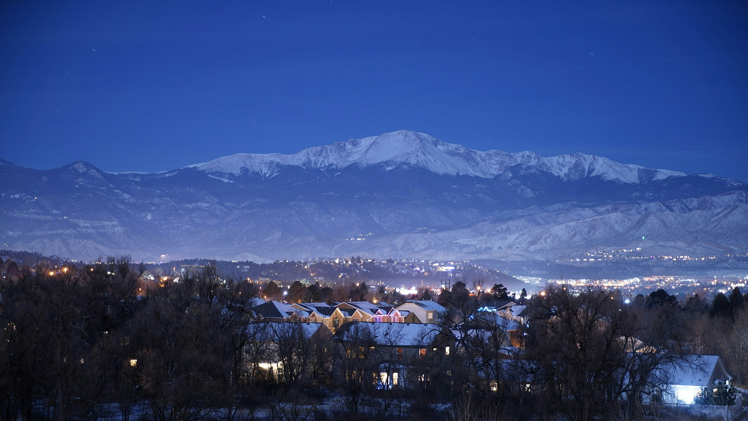 Captivating nighttime mountain view over a picturesque town, with softly lit homes and a serene snowy landscape.