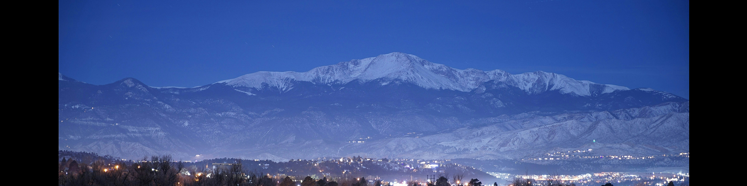 Charming neighborhood at night with snow-capped peaks, sparkling city lights, and serene winter landscape.