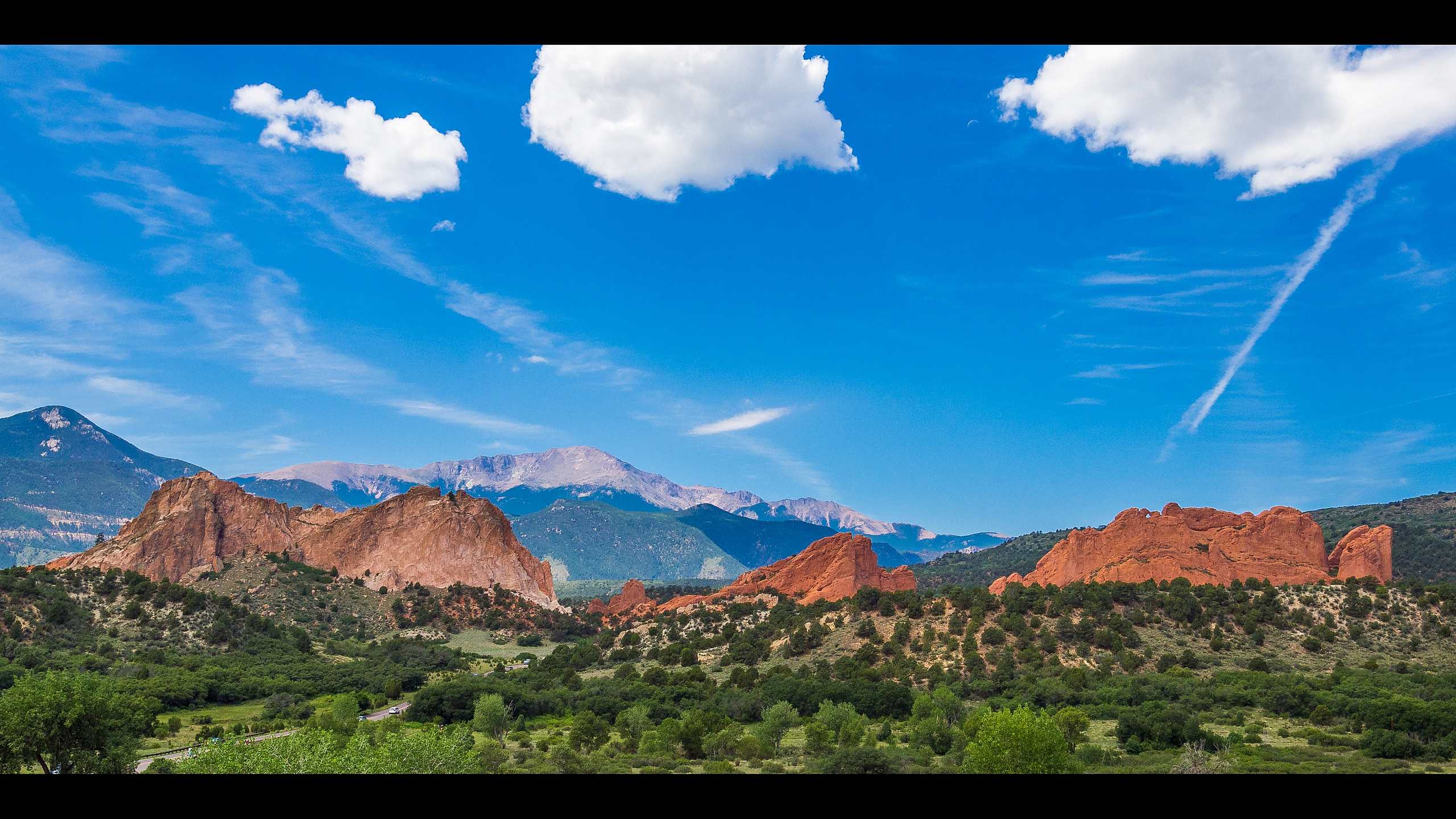 Breathtaking landscape of vibrant red rock formations under a bright blue sky, surrounded by lush greenery and majestic mountains.