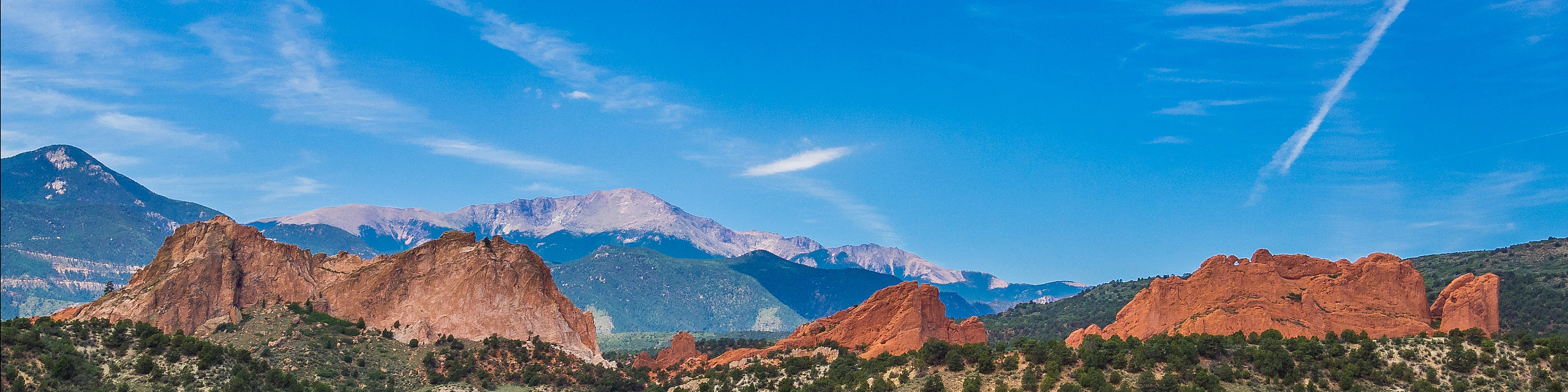 Breathtaking landscape with majestic red rock formations set against a clear blue sky and lush greenery.