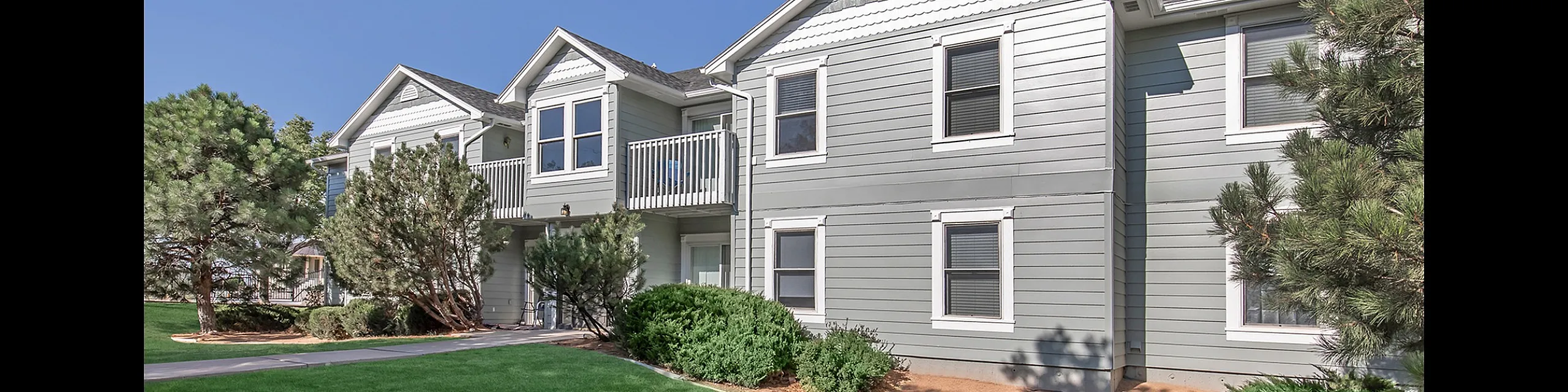 Charming apartment exterior with fresh gray siding, elegant white trim, and lush green landscaping, offering a peaceful and inviting residential atmosphere.