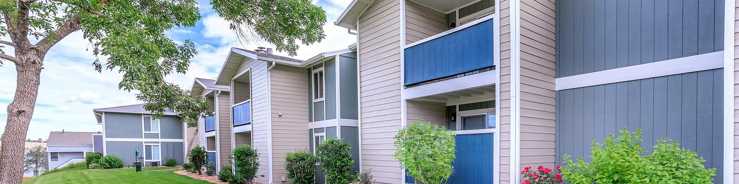 Charming apartment complex with lush green lawns, vibrant landscaping, and modern balconies in a serene setting.