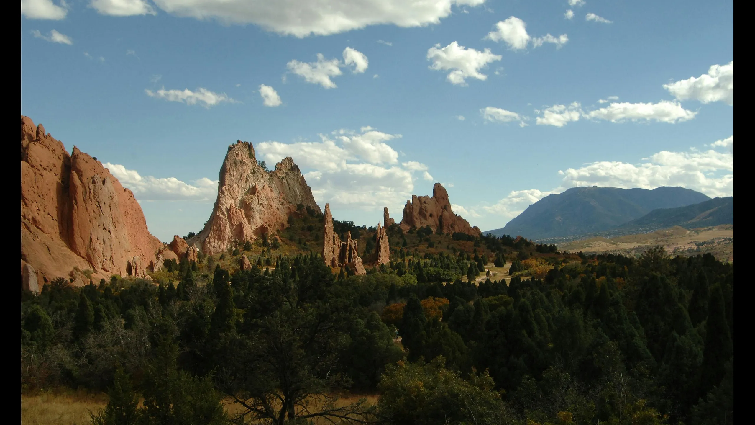 Breathtaking landscape featuring striking red rock formations under a vibrant blue sky with fluffy clouds, surrounded by lush greenery.