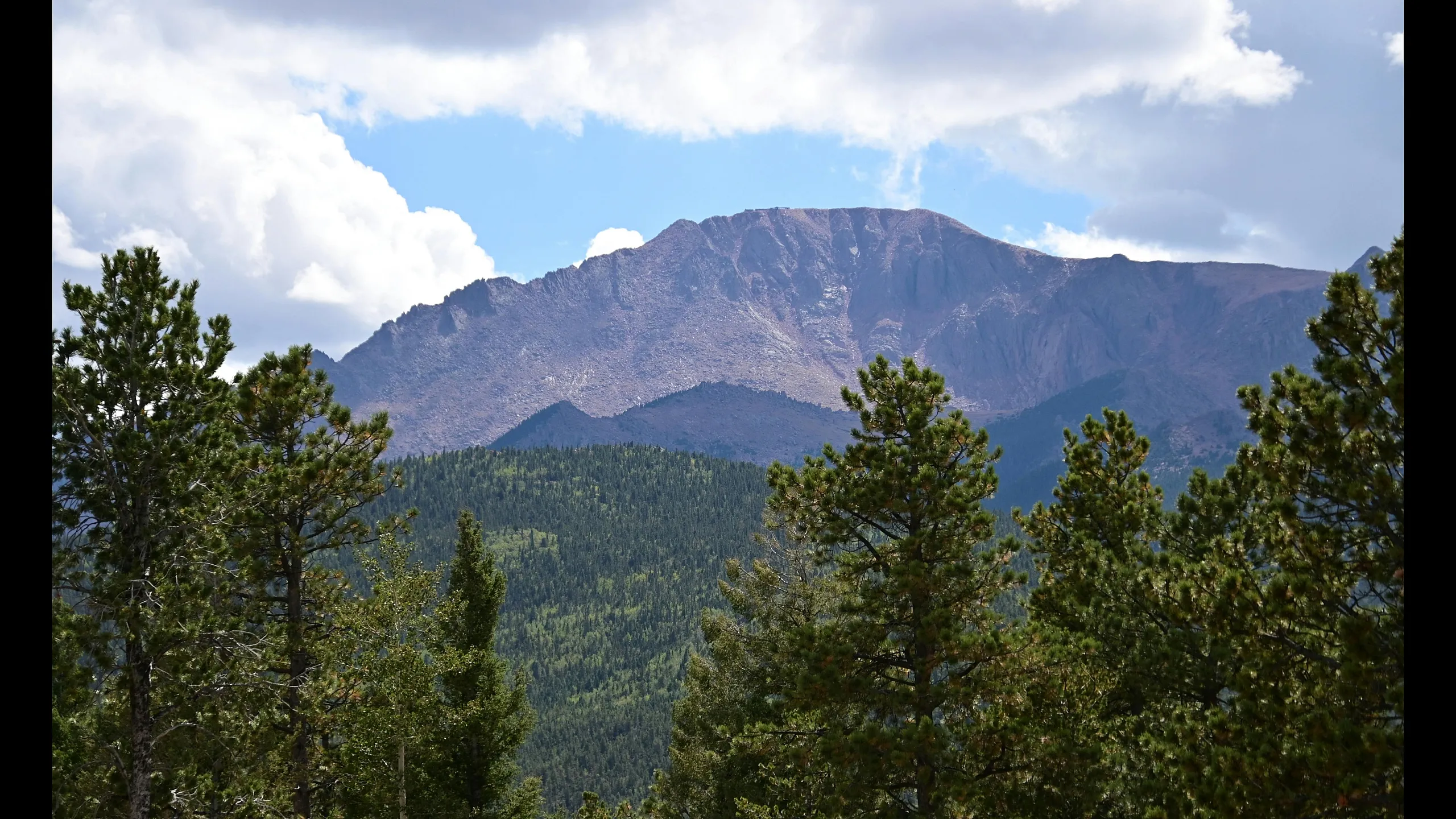 Breathtaking mountain view with lush green forests and a stunning peak under a vibrant blue sky.