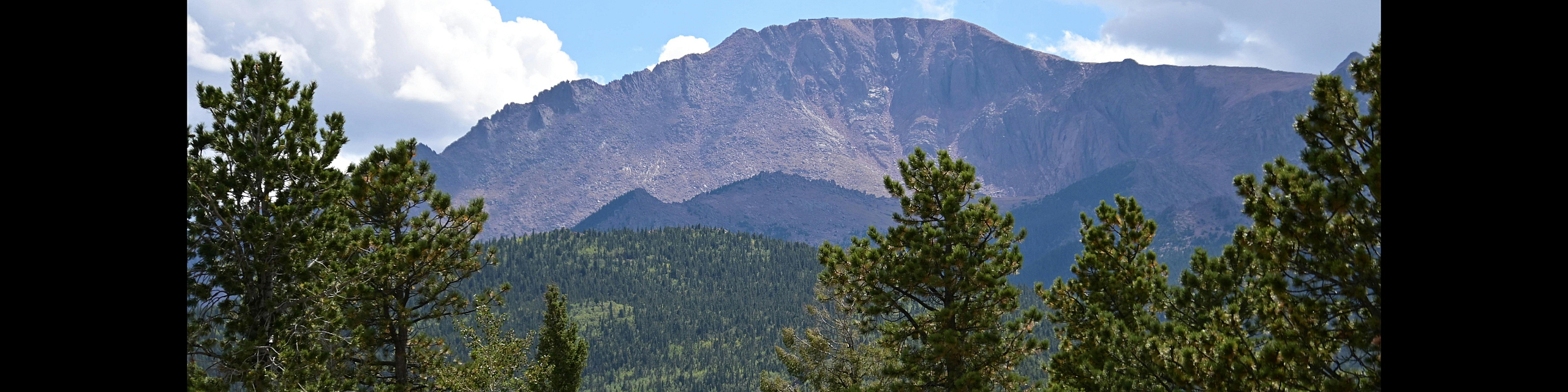 Breathtaking view of a majestic mountain peak surrounded by lush green forests under a vibrant blue sky.
