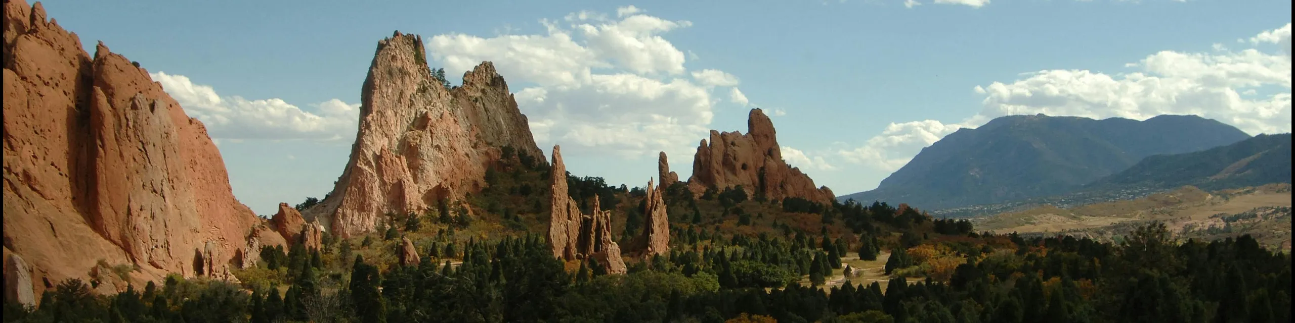 Breathtaking scenic view of majestic red rock formations under a clear blue sky, surrounded by lush greenery and distant mountains.