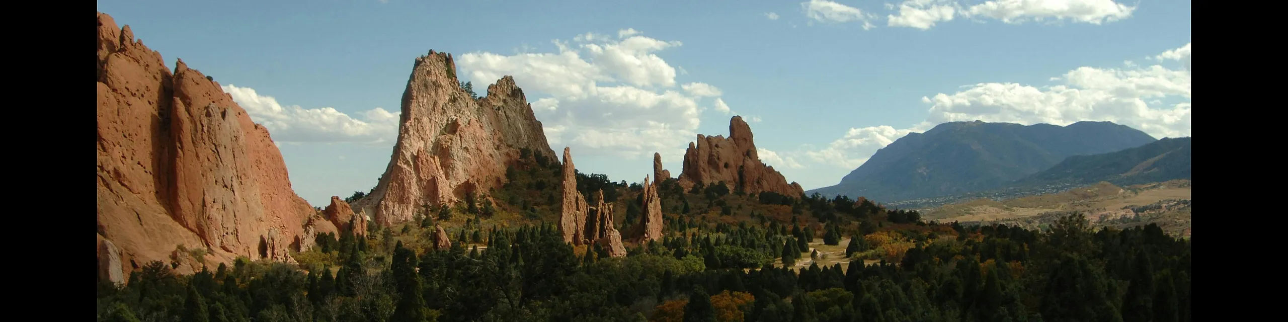 Breathtaking view of towering red rock formations surrounded by lush greenery and a vast, clear blue sky, capturing nature's grandeur.