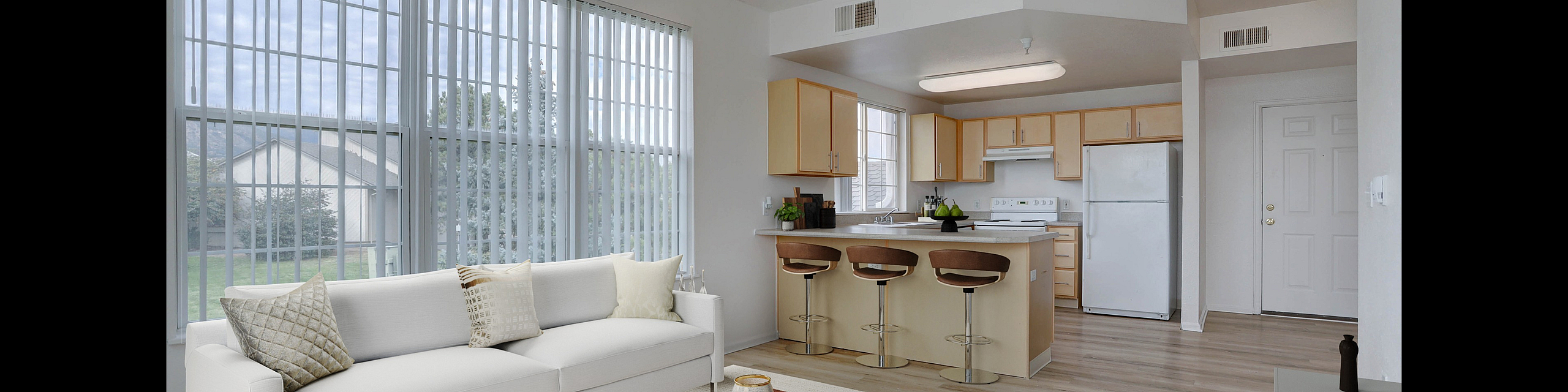 Bright and modern open-concept living room featuring large windows, sleek kitchen with bar seating, and elegant decor.