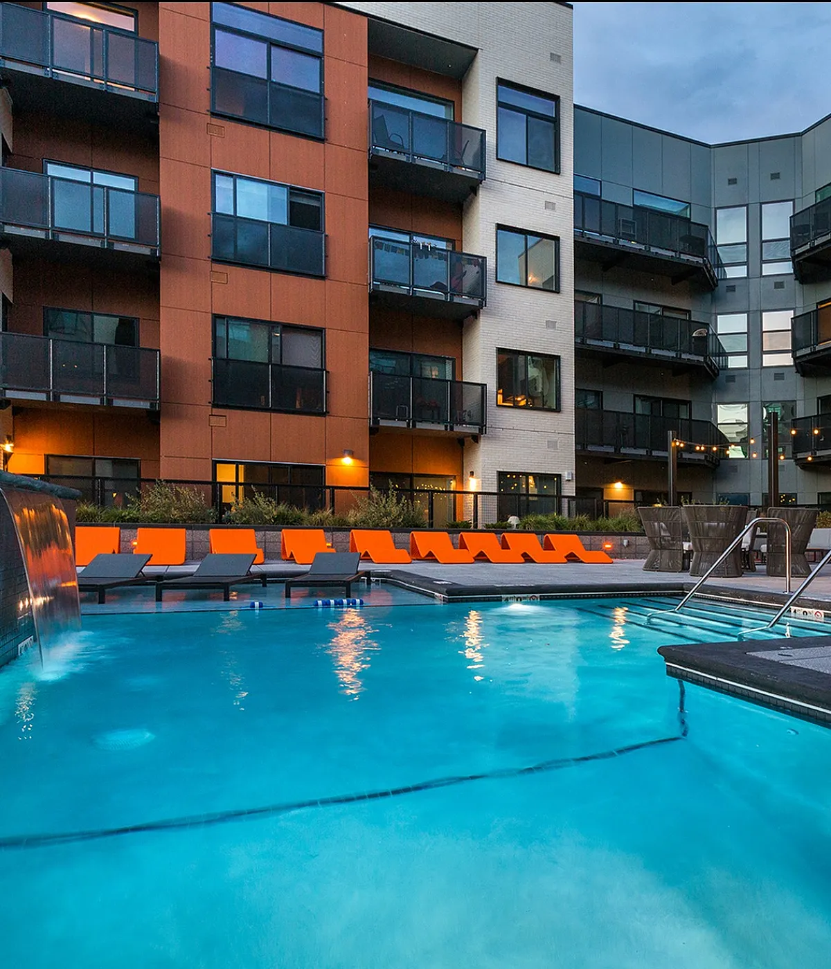 Modern apartment complex with a luxurious outdoor pool and stylish lounge chairs, offering a perfect blend of comfort and sophistication.