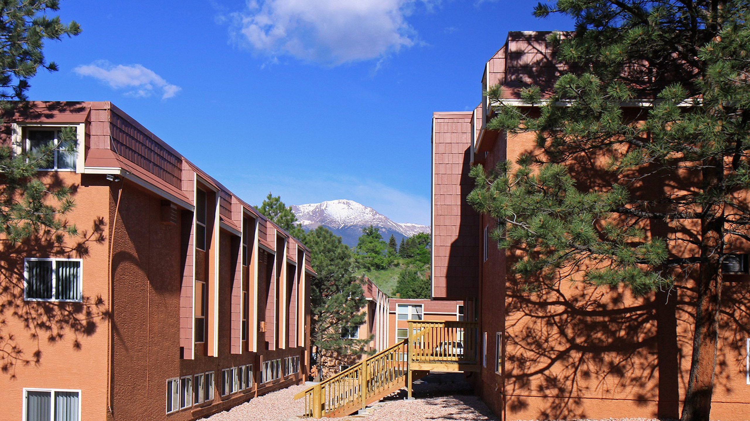Stunning apartment exterior with red brick buildings, nestled amidst lush greenery, offering scenic mountain views and clear blue skies.
