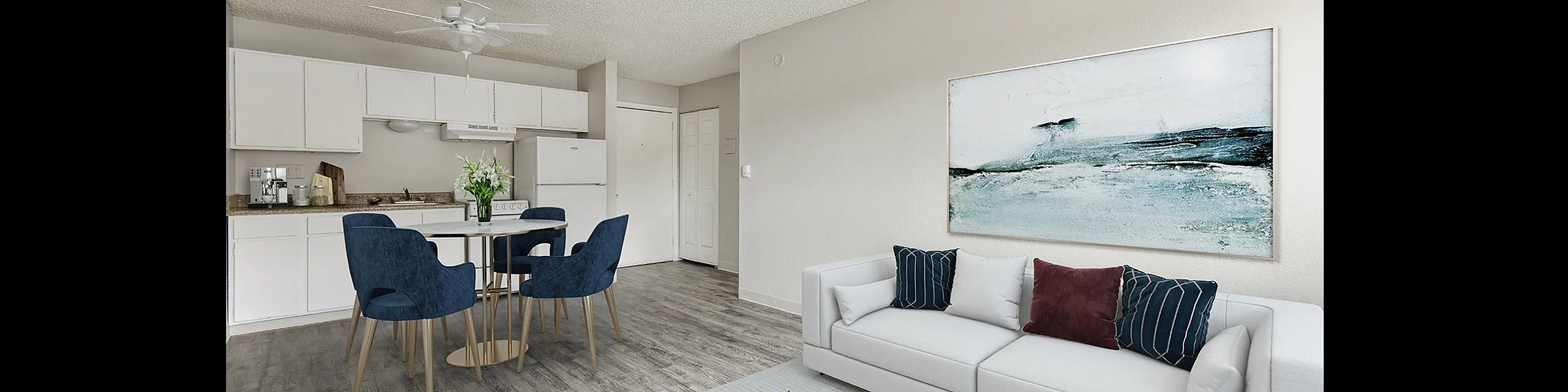 Modern apartment interior featuring an elegant open-plan layout with a sleek white kitchen, cozy dining area with blue velvet chairs, and a stylish living room with contemporary artwork and plush white sofa.