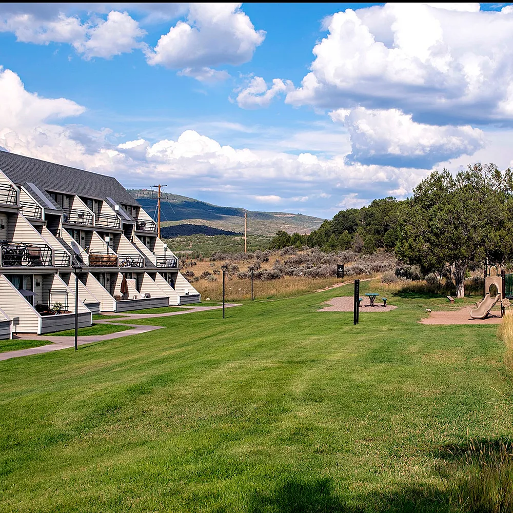 Charming residential complex with unique architecture set against a serene landscape, featuring lush green lawns and a playground, offering an ideal family-friendly environment.