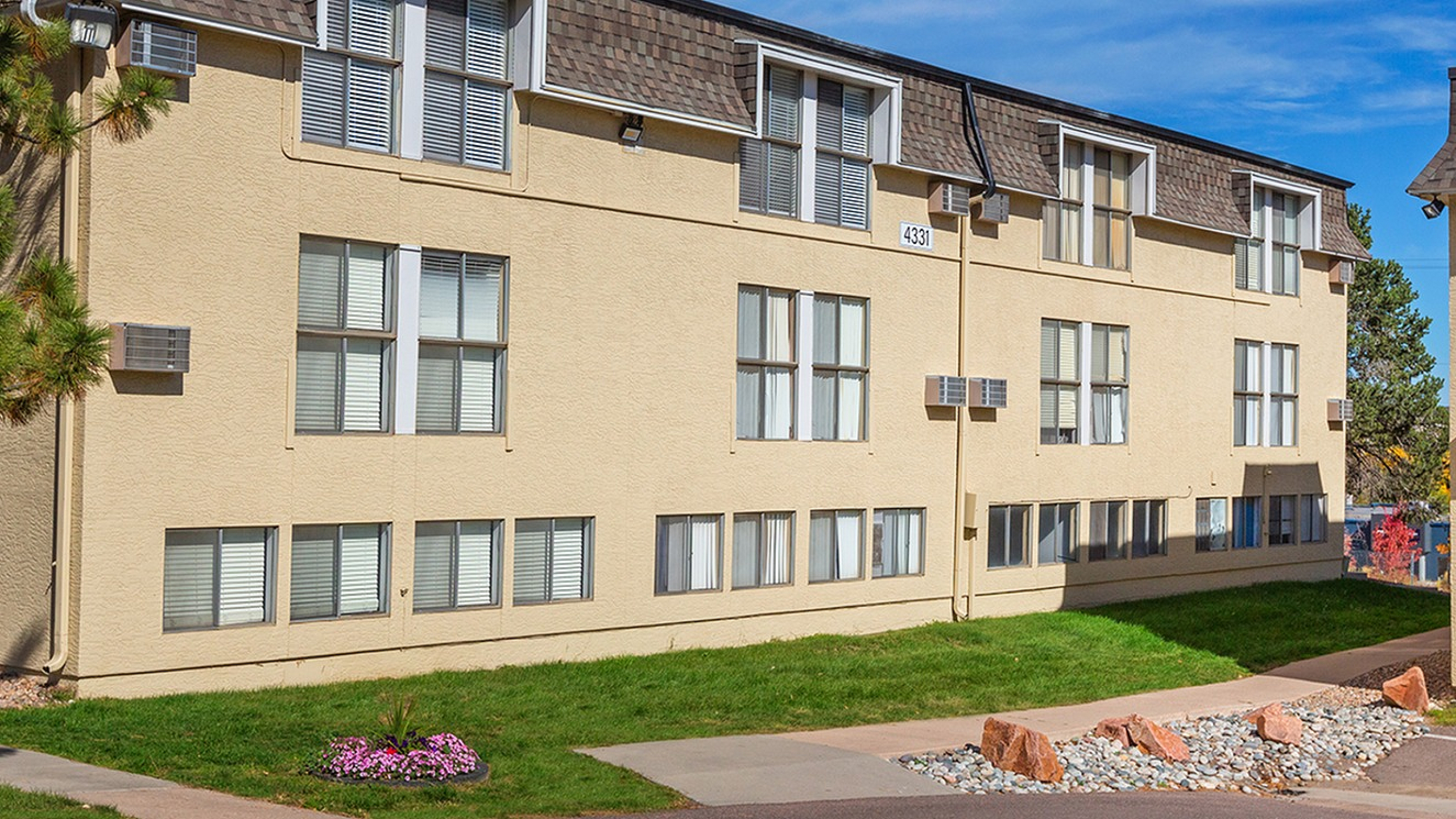 Charming apartment building with modern design, featuring large windows and well-maintained landscaping under a clear blue sky.