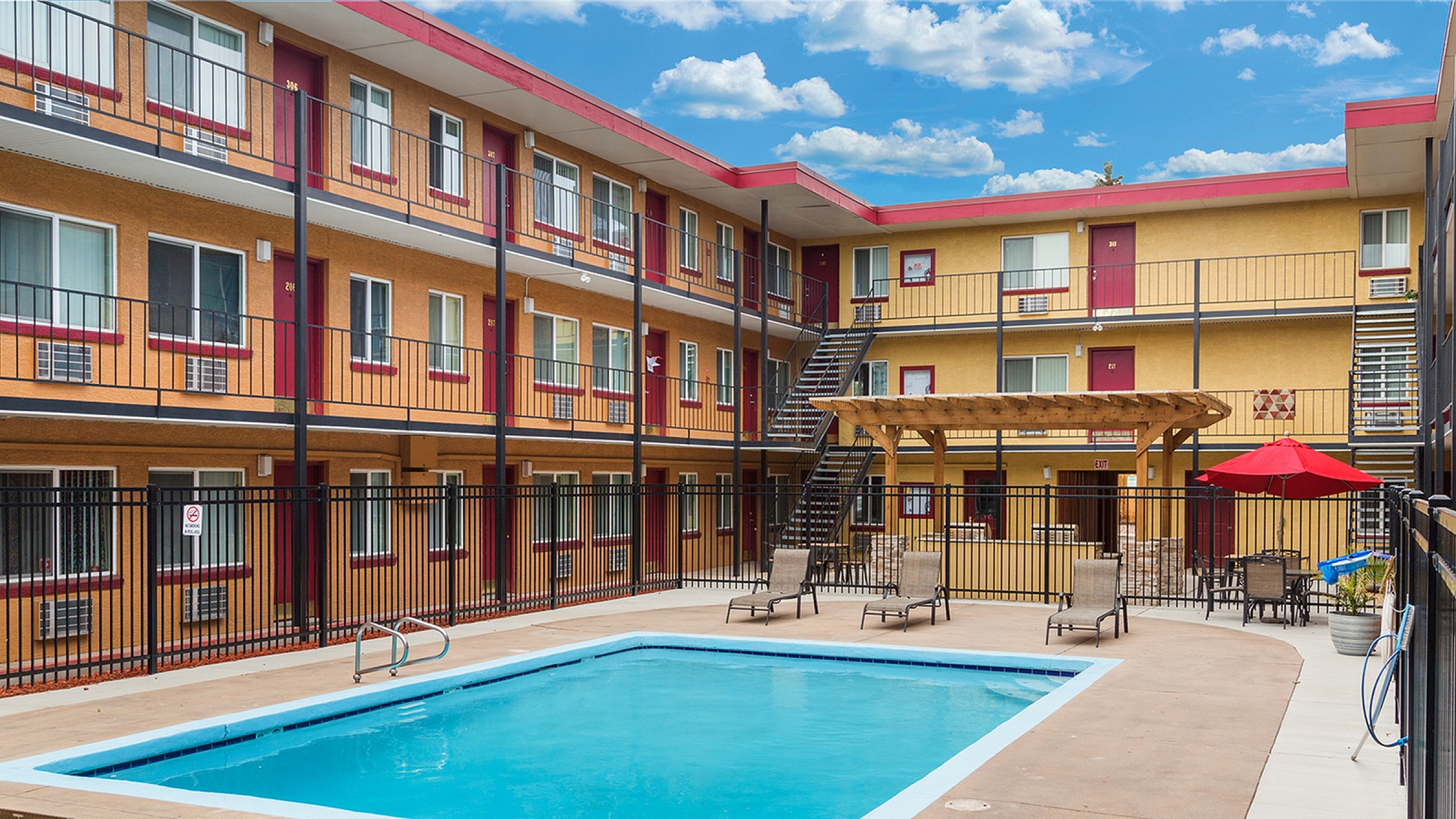 Charming apartment complex with inviting outdoor swimming pool, stylish sun loungers, and vibrant umbrellas under a clear blue sky.