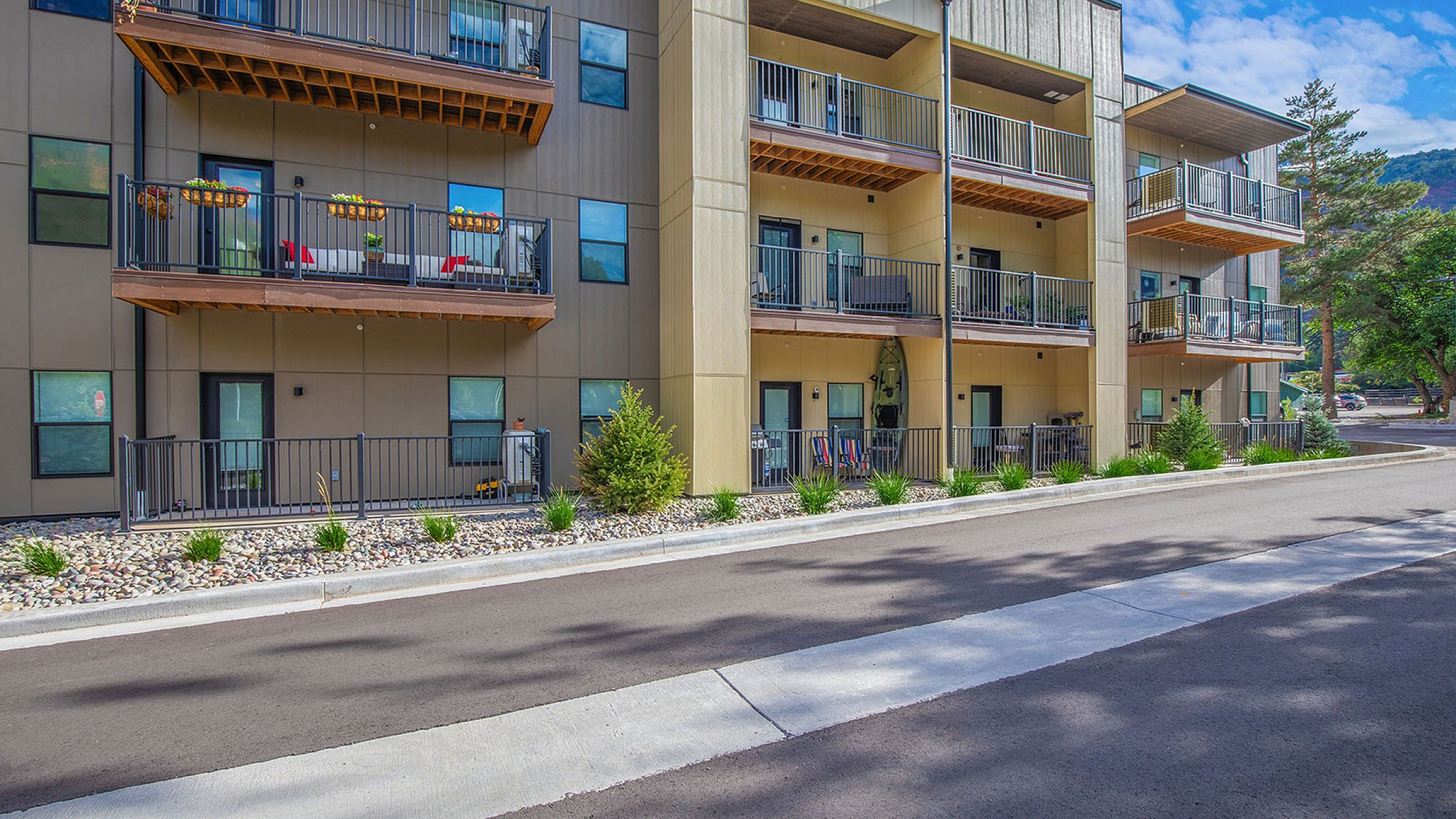 Contemporary apartment building with stylish balconies, surrounded by lush greenery and scenic views.