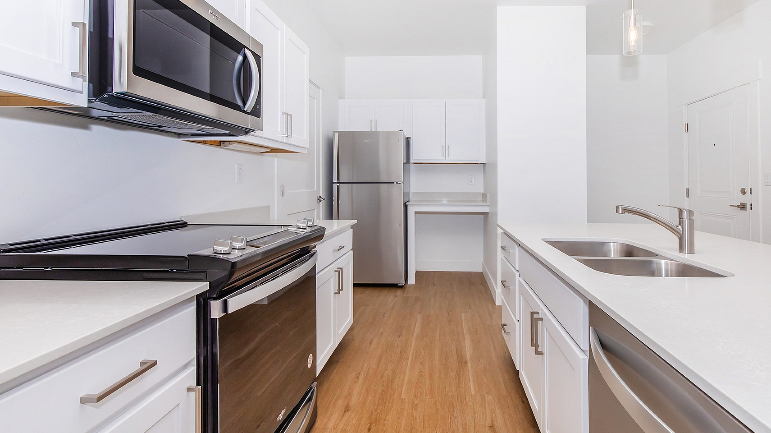 Bright, modern kitchen featuring sleek stainless steel appliances, elegant white cabinetry, and spacious quartz countertops with wood flooring.