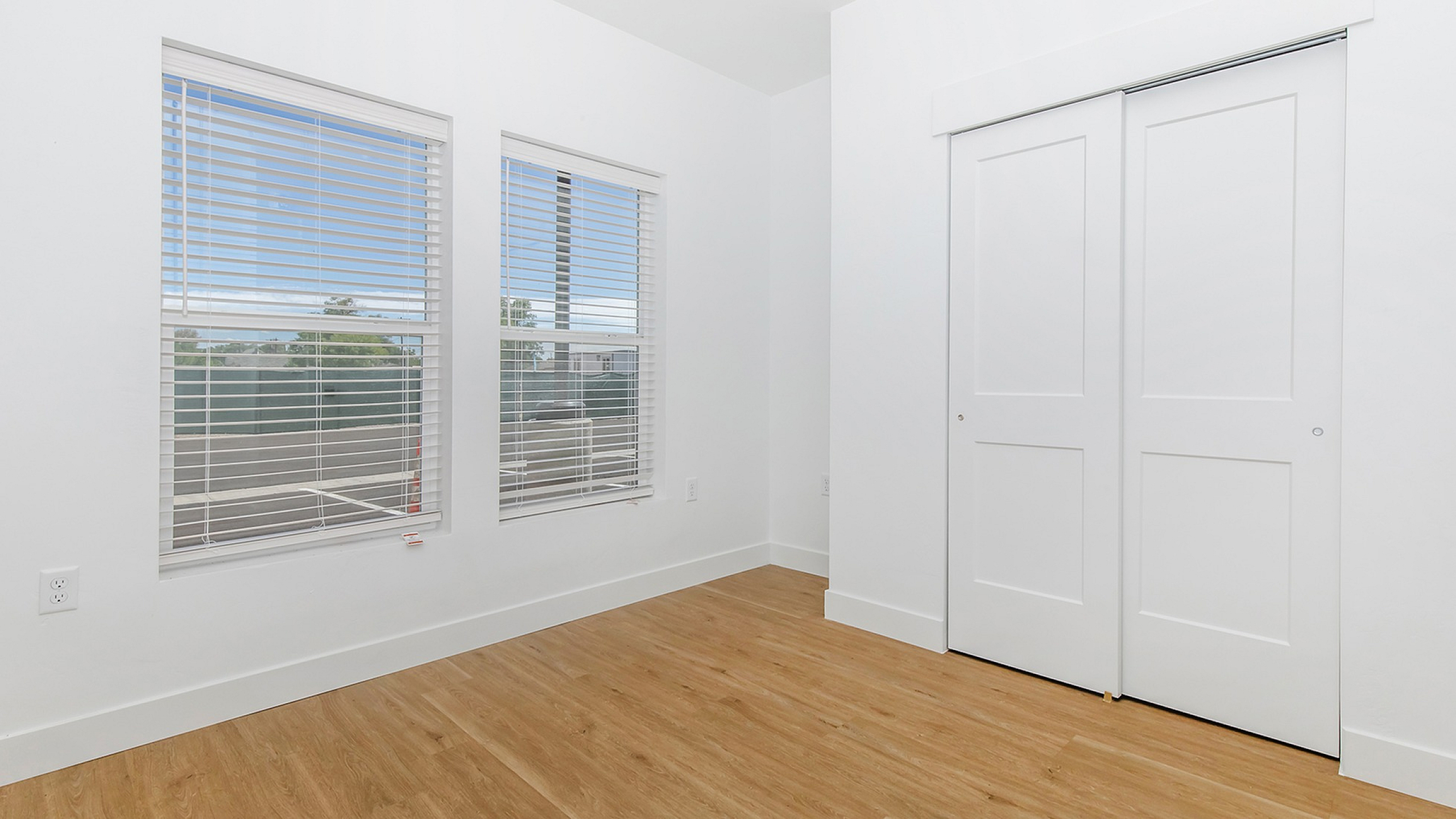 Bright and inviting empty room with large windows, sleek wooden flooring, and a spacious closet, perfect for personalization and comfort.