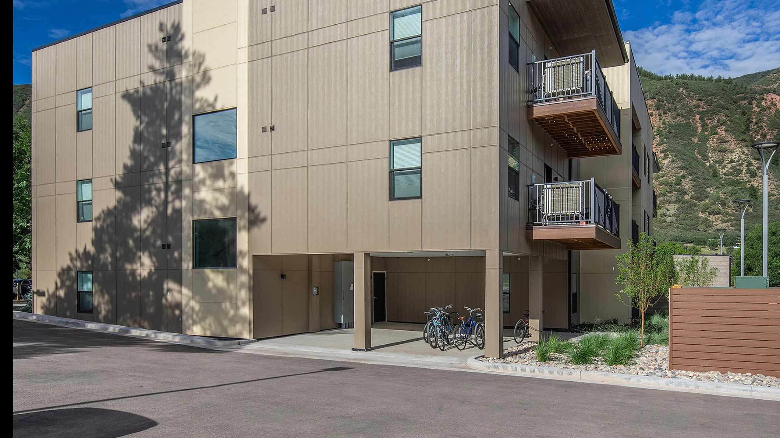 Modern apartment building exterior with balconies, set against a scenic mountain backdrop, includes convenient bike parking.