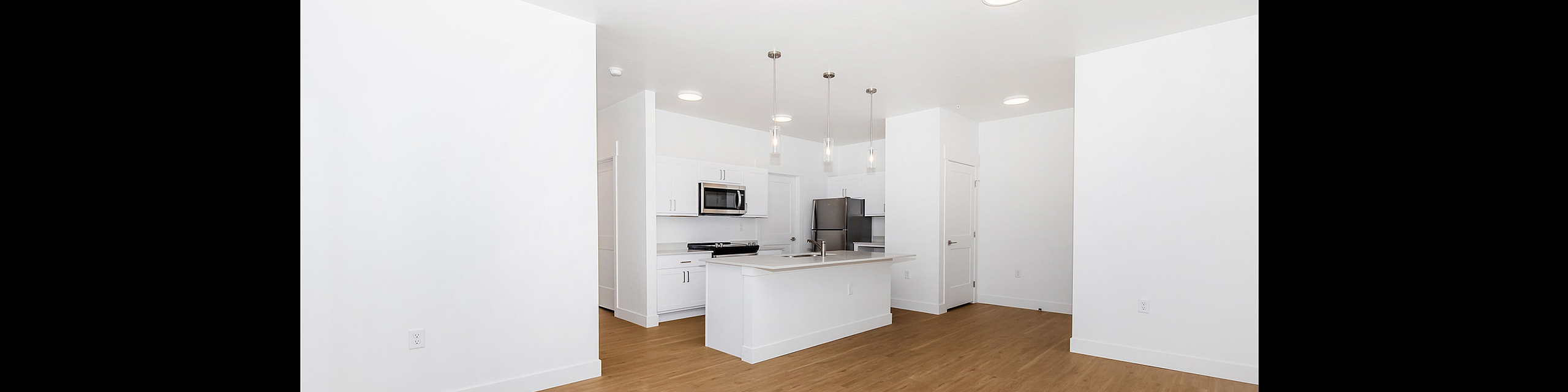 Modern open-concept kitchen with sleek white cabinetry, stainless steel appliances, and hardwood flooring, offering a spacious and bright living area.