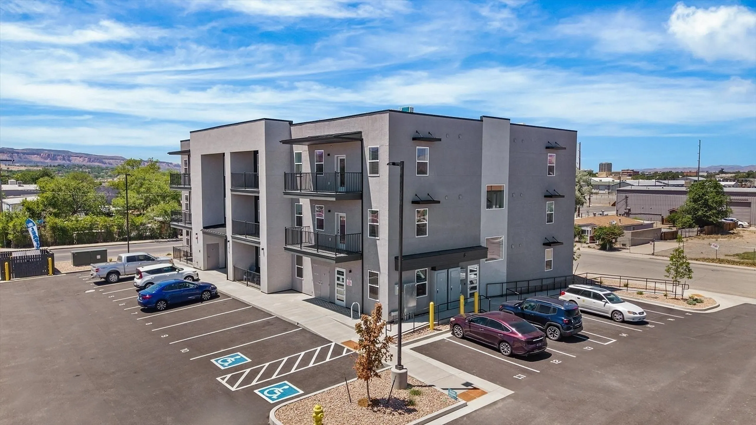 Modern apartment building with spacious balconies, ample parking, and vibrant views of surrounding landscape under a clear blue sky.