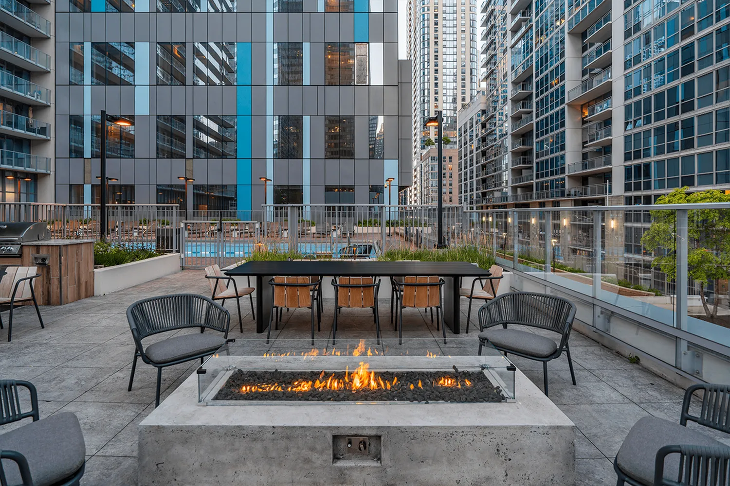 Chic apartment patio with cozy fire pit, elegant seating, and a view of urban high-rises.