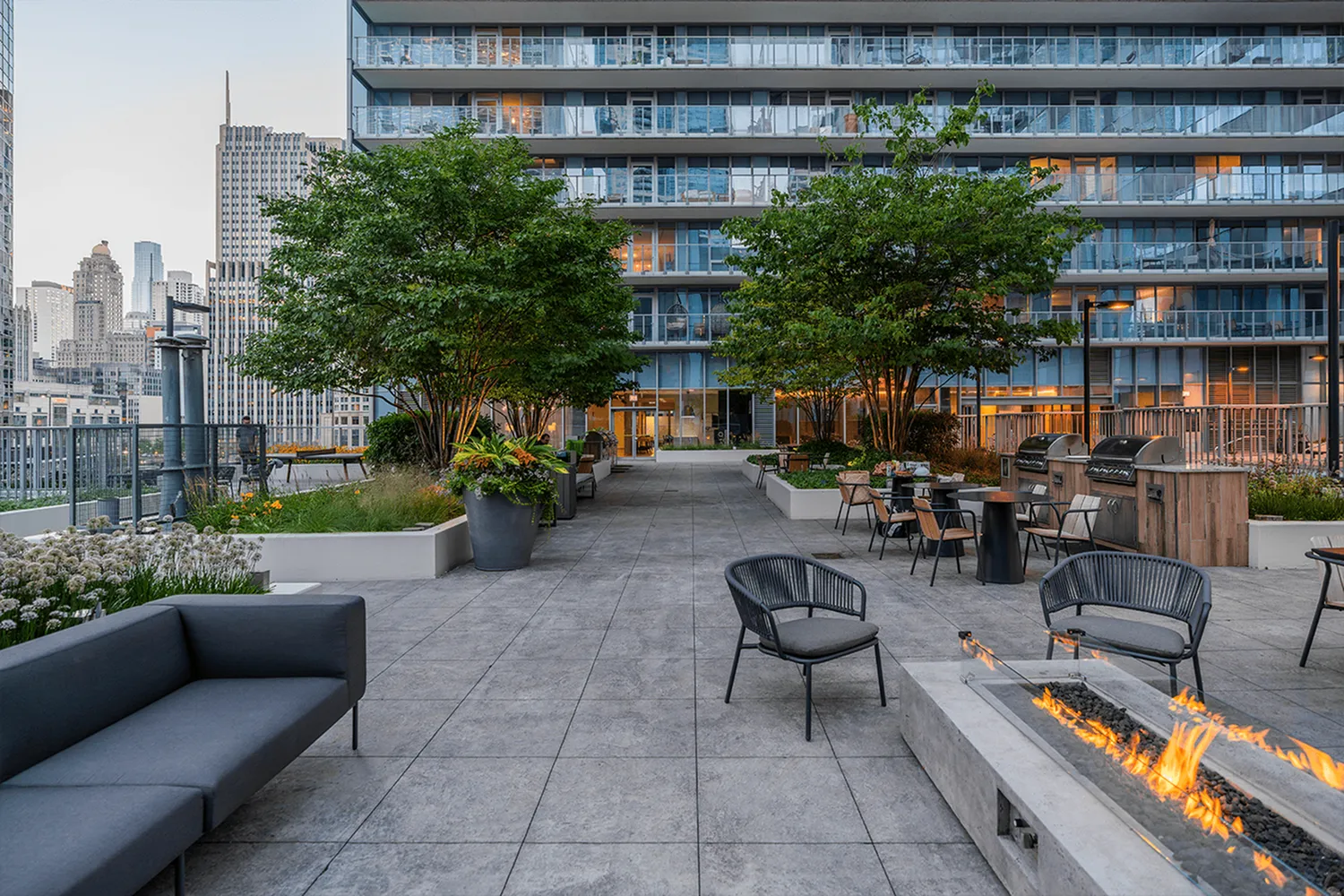 Luxurious apartment terrace with modern seating, fire pit, and city skyline views.