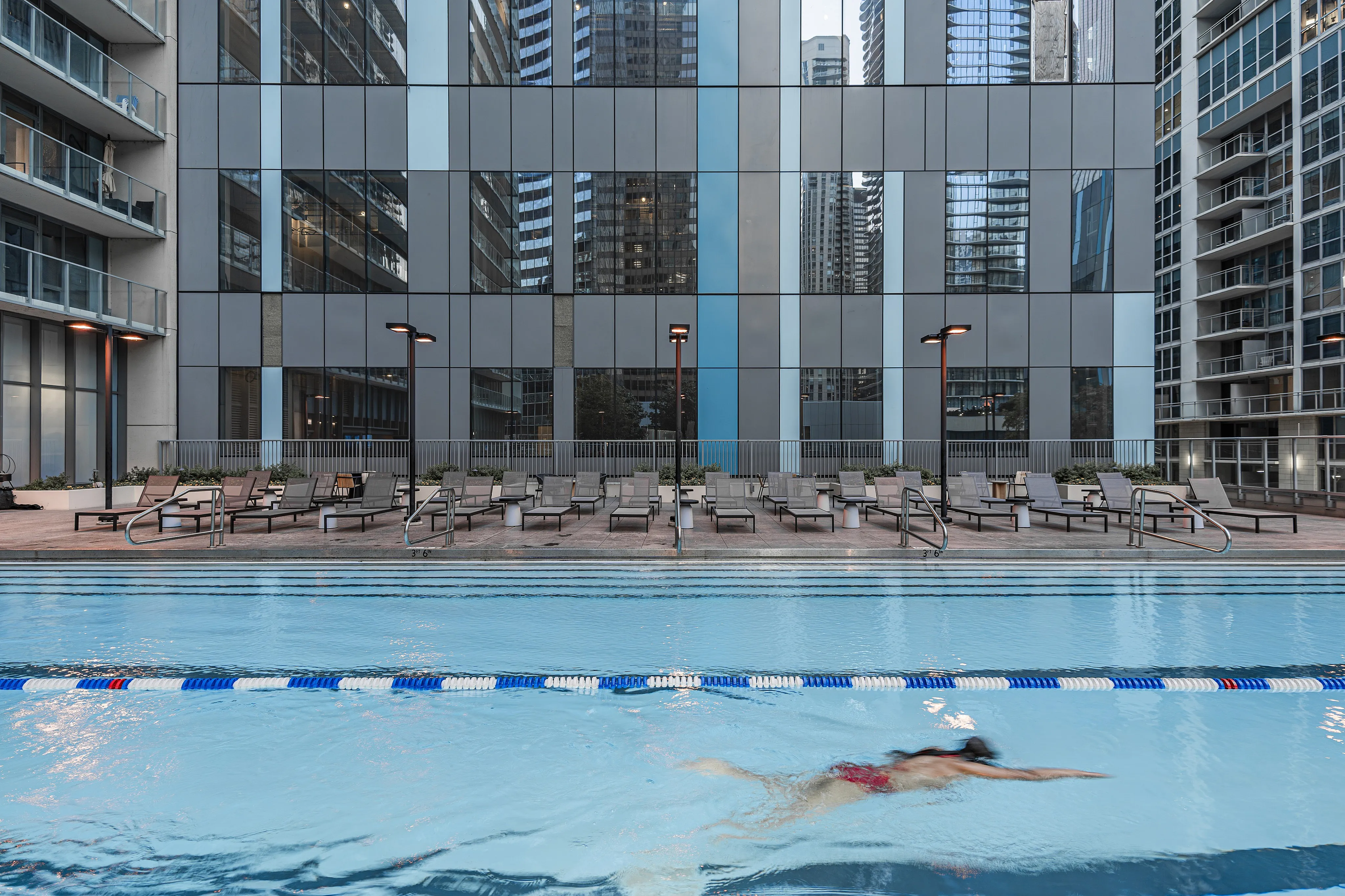 Modern urban swimming pool with sleek sun loungers, surrounded by high-rise architectural marvels. A serene oasis for relaxation and leisure.