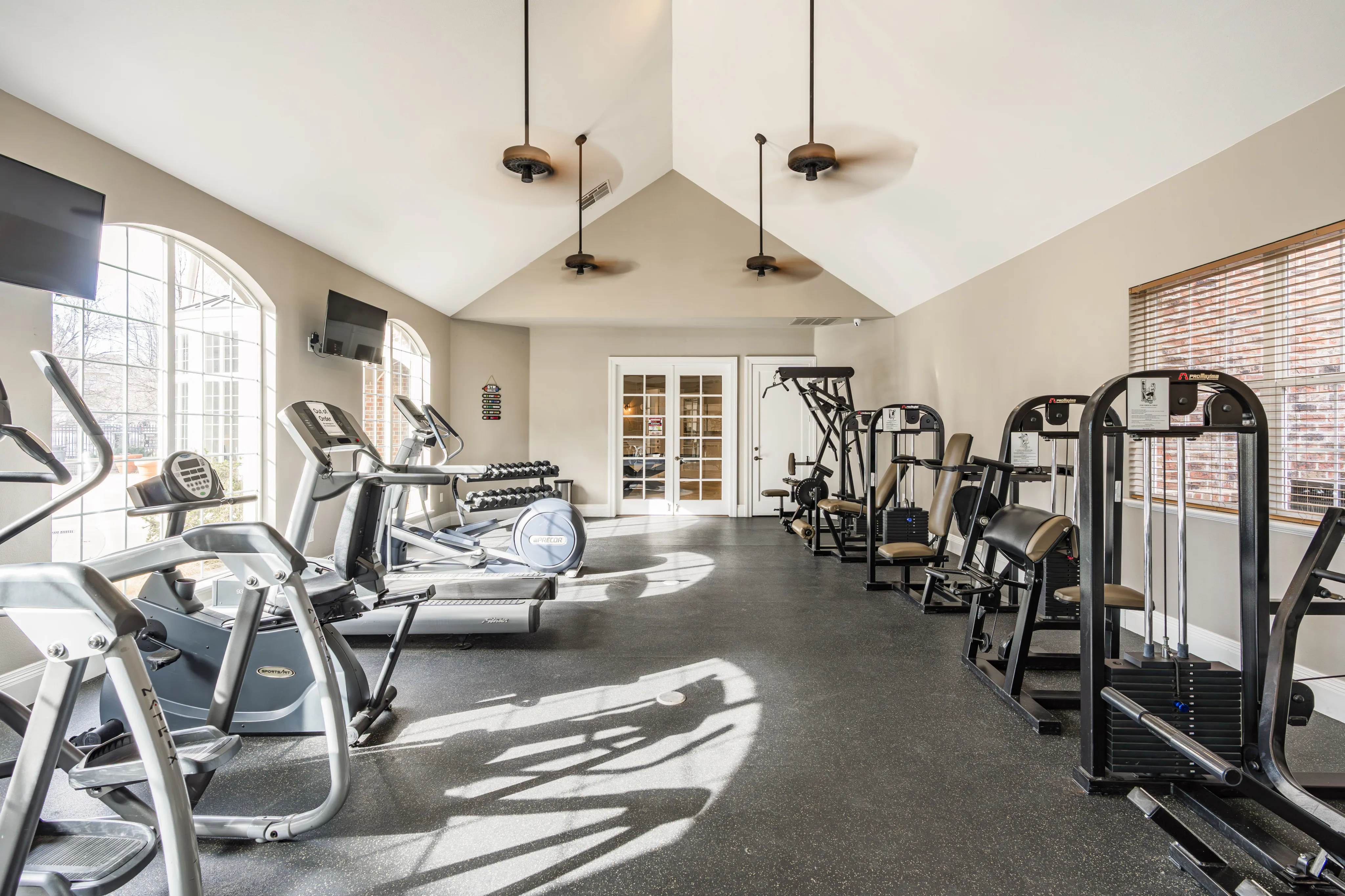 Bright and modern fitness center featuring state-of-the-art cardio and strength equipment, accented by large arched windows and elegant lighting.