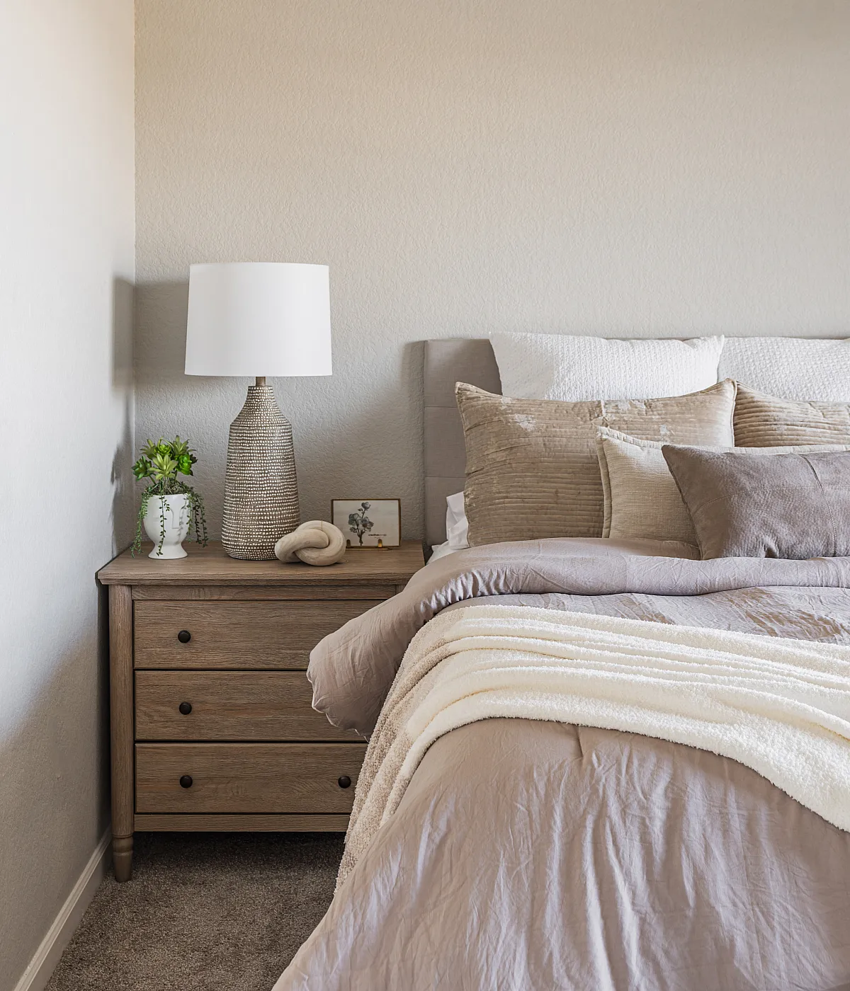 Cozy bedroom with elegant neutral tones, featuring a plush bed, stylish wooden nightstand, and soft ambient lighting.