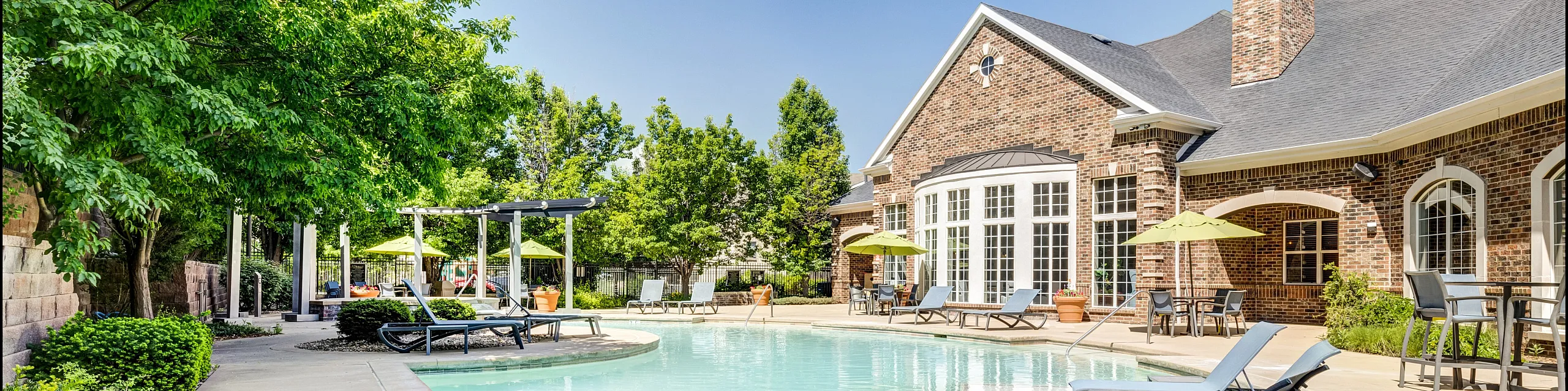 Luxurious apartment complex featuring a pristine swimming pool, lush greenery, and elegant brick architecture for an upscale living experience.