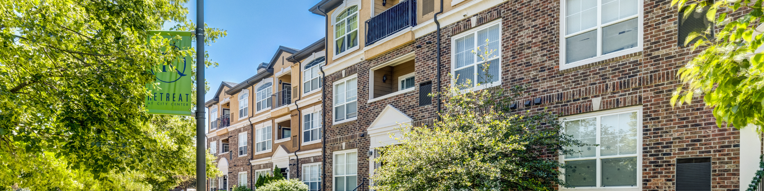 Charming apartment building with classic brick facade, surrounded by lush greenery and bathed in natural sunlight.