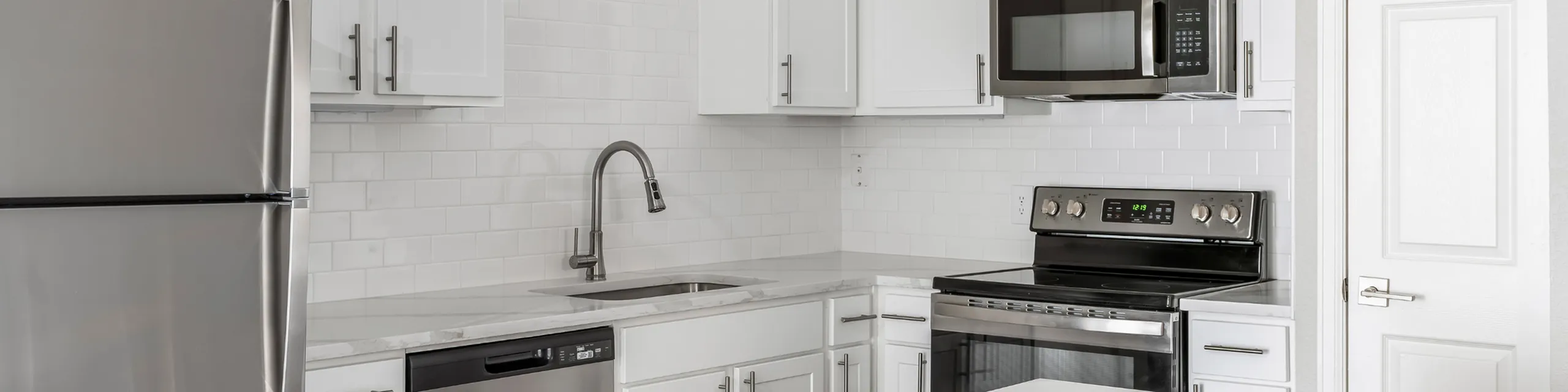 Modern kitchen with sleek stainless steel appliances, white cabinetry, and pristine subway tile backsplash.