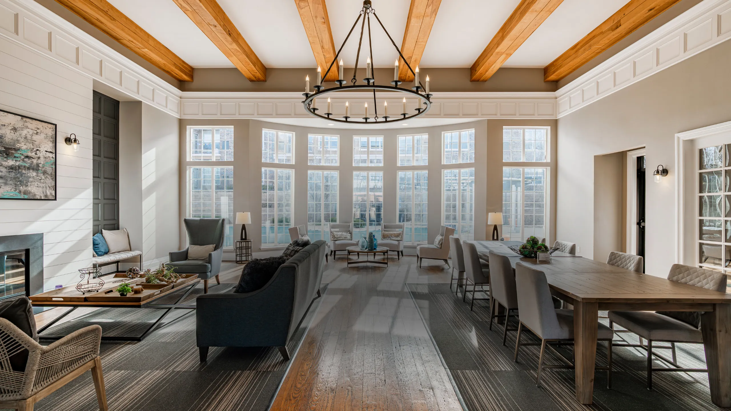 Elegant living room with vaulted ceilings, large windows, and cozy seating area, featuring exposed wooden beams and a grand chandelier.