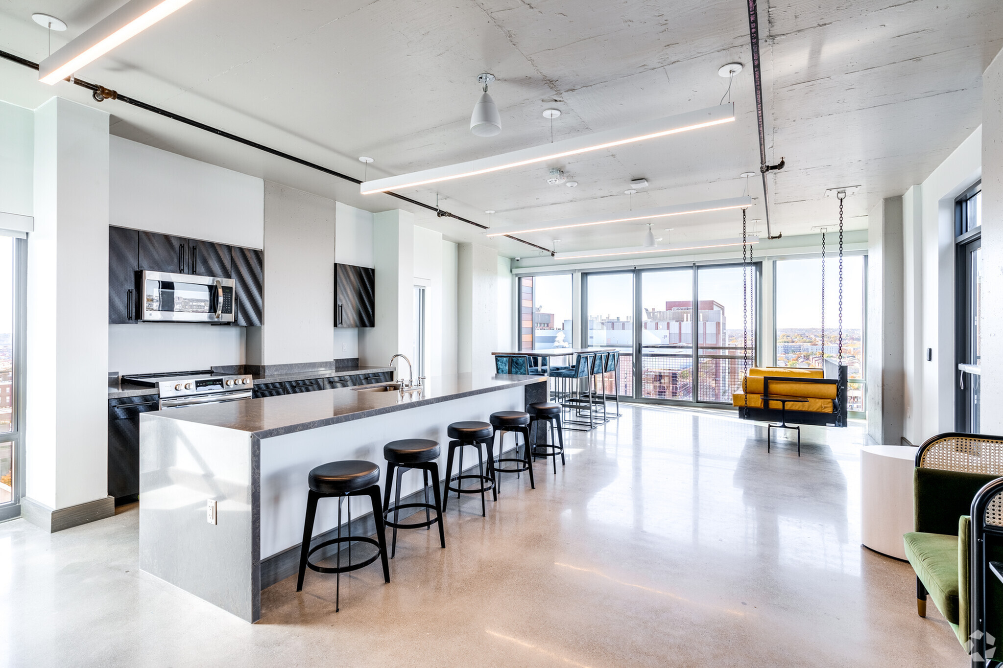 Modern open-concept apartment with a sleek kitchen, stylish bar area, and inviting swing seating, bathed in natural light from floor-to-ceiling windows.