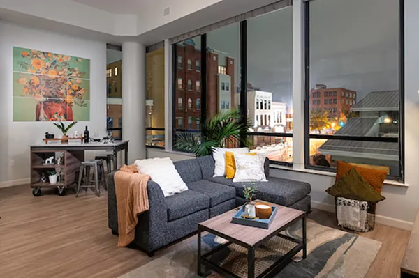 Chic urban apartment living room with modern decor, large windows showcasing vibrant city views, and cozy seating area for relaxation.