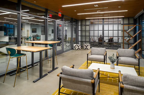 Modern office space with cozy seating area, vibrant decor, and sleek glass walls, perfect for collaborative work.