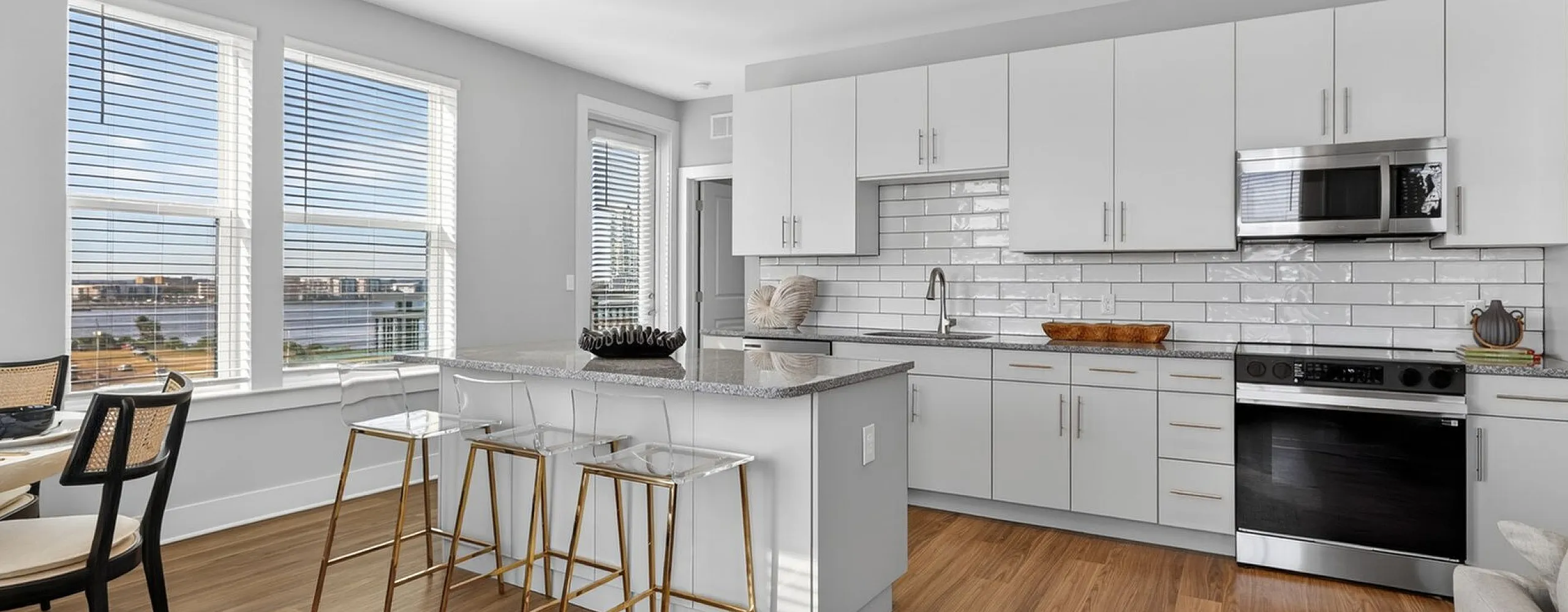 Bright, modern kitchen with sleek white cabinetry, a spacious island with gold-accented stools, and large windows offering stunning city views.
