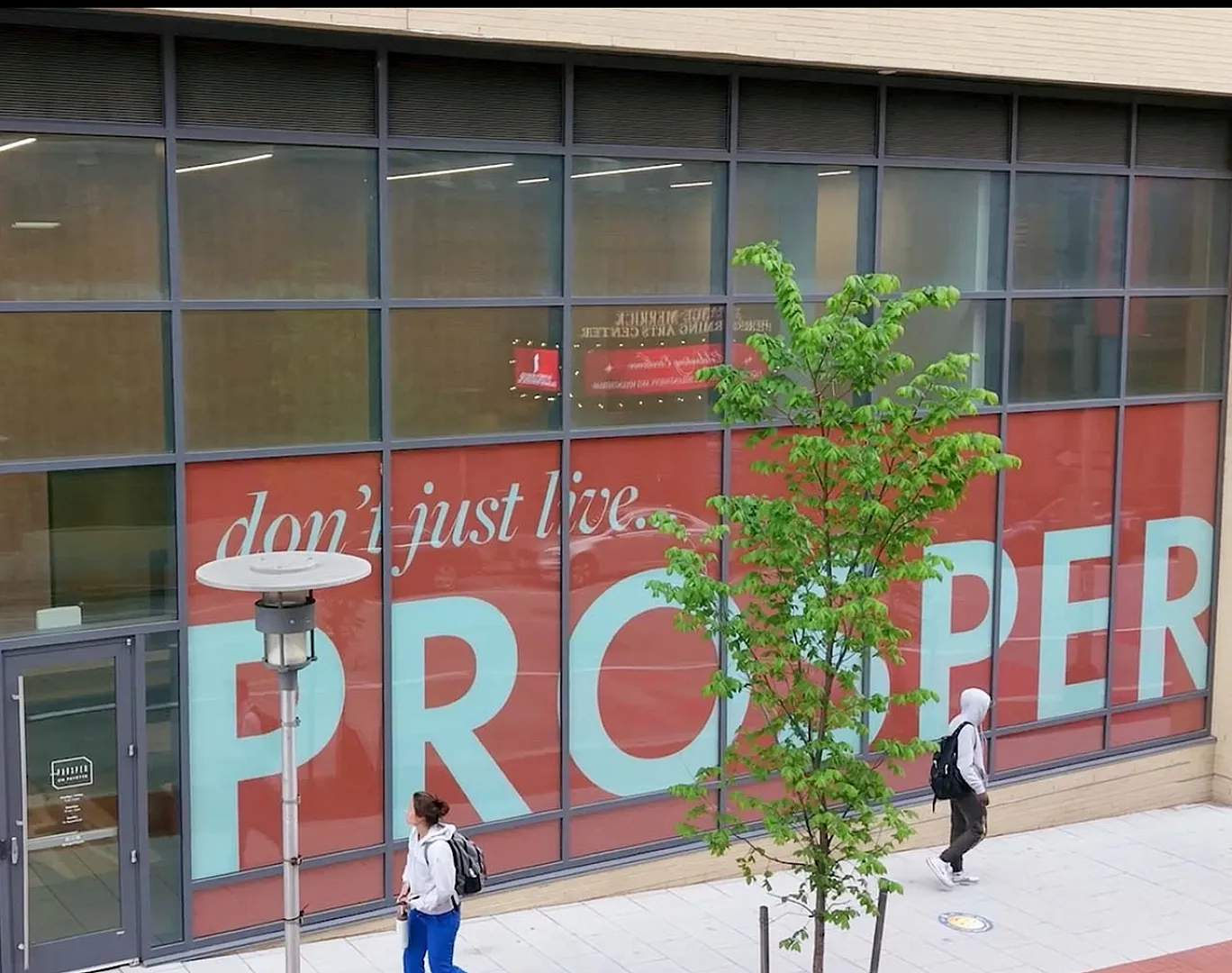 Vibrant urban street view showcasing modern architecture with large windows and inviting signage that reads 'Don't just live, PROSPER.'