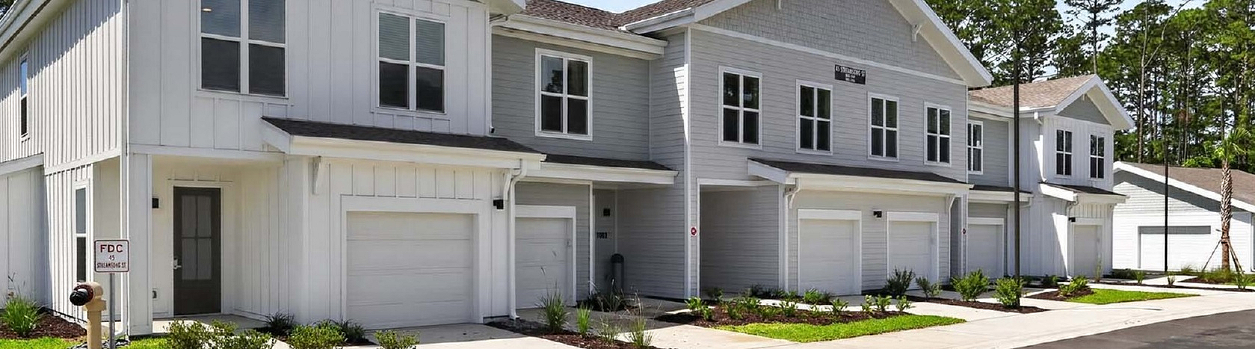 Modern townhouse row with charming facades and lush landscaping under a clear blue sky.