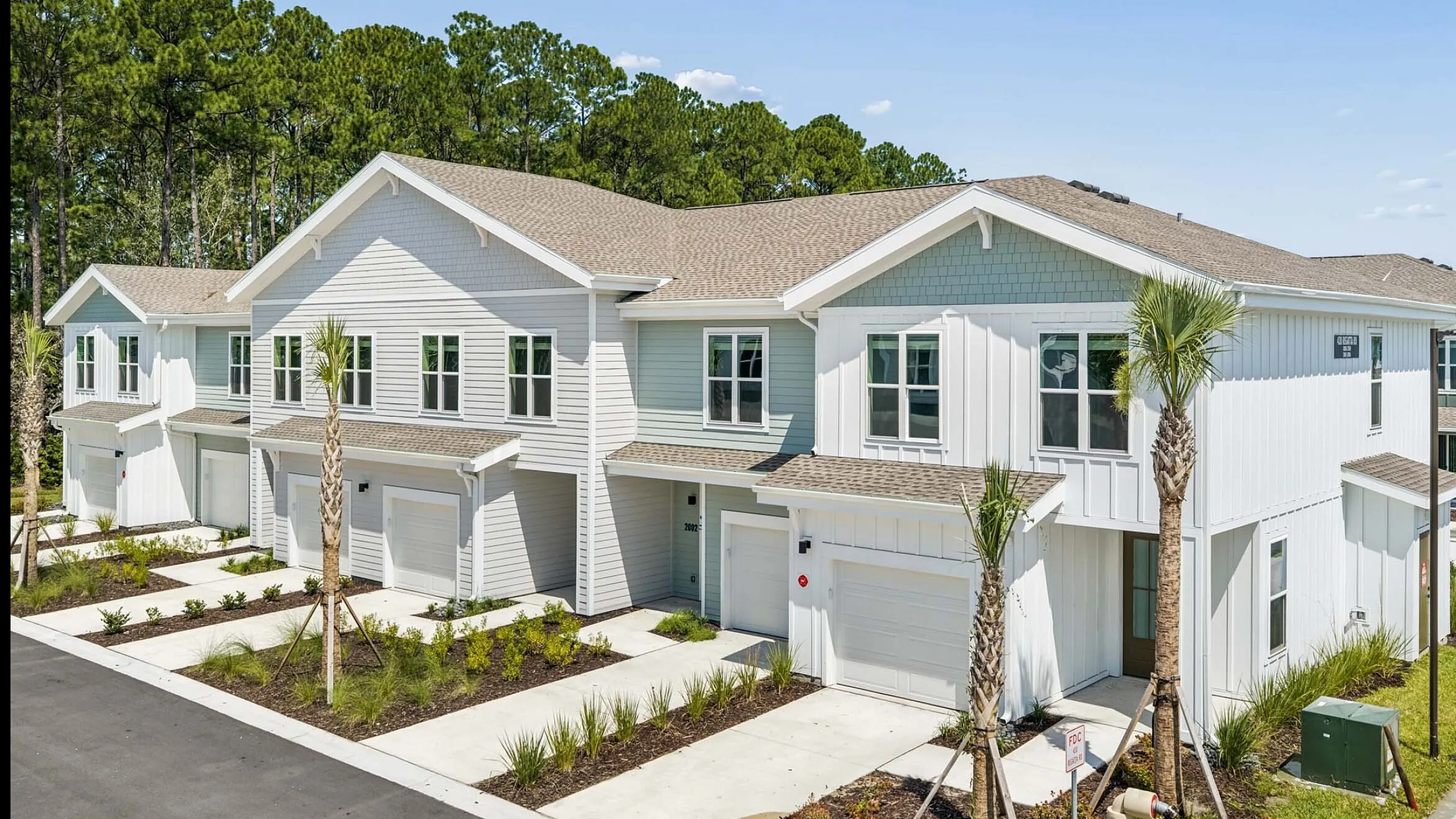 Charming townhouse row with modern architecture, featuring lush landscaping, spacious garages, and surrounded by tranquil greenery.