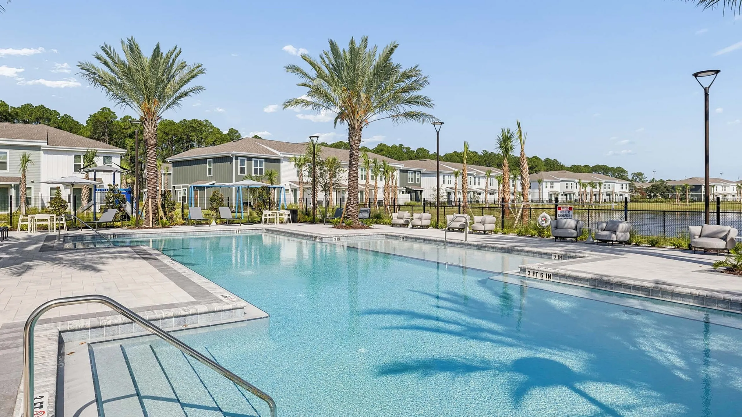 Inviting outdoor pool area surrounded by lush palm trees and modern townhouses, offering a serene and luxurious retreat.