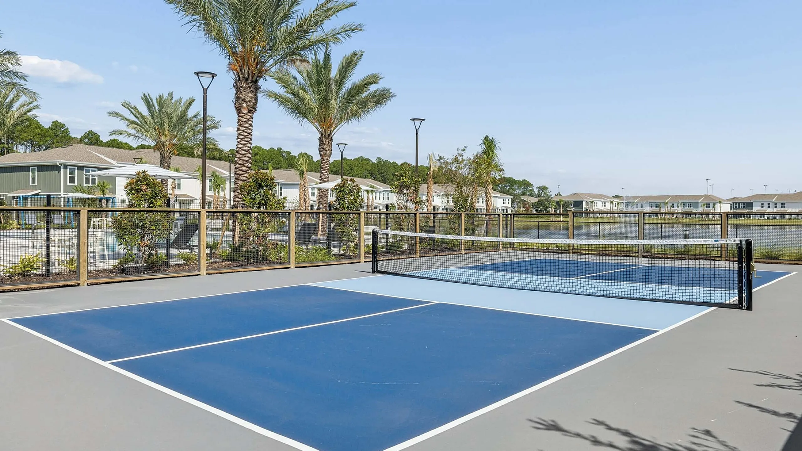 Luxurious apartment complex surrounded by palm trees, featuring a modern tennis court and serene water views.