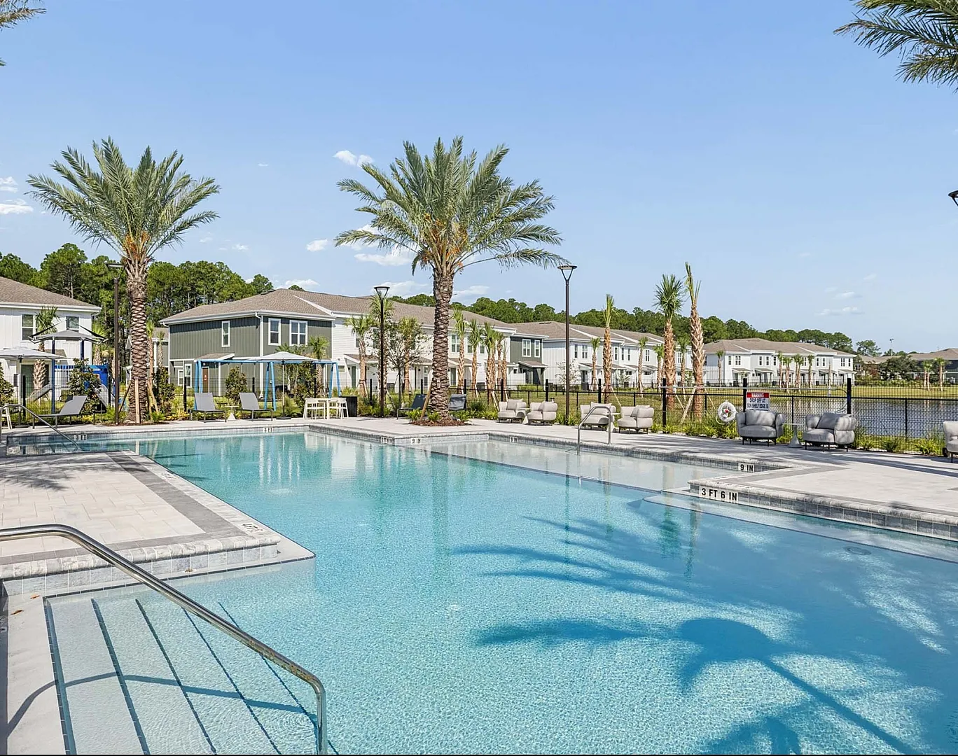 Luxurious community pool surrounded by palm trees and modern townhouses, offering a serene oasis for relaxation and leisure.