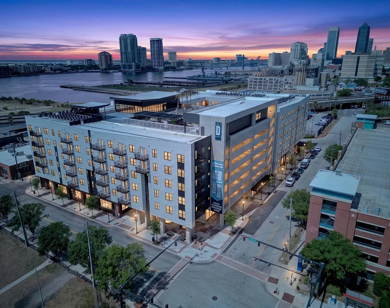 Stunning modern apartment complex at dusk with city skyline and river views, featuring well-lit interiors and balconies.
