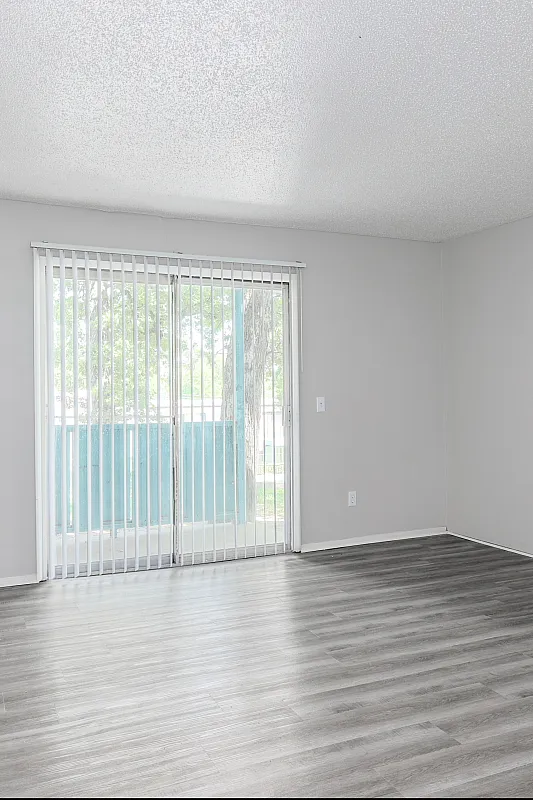 Bright living space with modern vinyl flooring and a large window leading to a balcony, offering a fresh and open atmosphere.