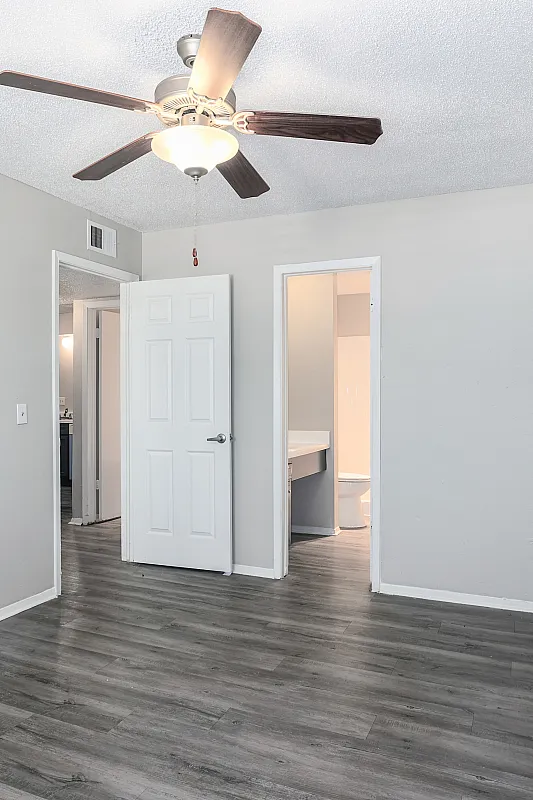 Modern bedroom with sleek wooden flooring, ceiling fan, and ensuite view, offering comfort and style.